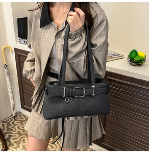 Detail of a black textured baguette bag with silver buckle worn with a beige suit