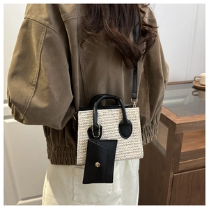 Close-up of beige woven texture crossbody bag with black handles and small hanging pouch