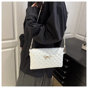 Détail du sac bandoulière matelassé blanc avec nœud doré et fermeture zippée discrète