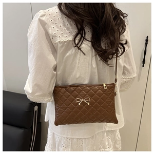Détail du sac matelassé marron avec nœud doré porté sur une robe en dentelle blanche