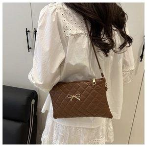 Sac à bandoulière matelassé marron avec nœud doré porté par un modèle en intérieur chic