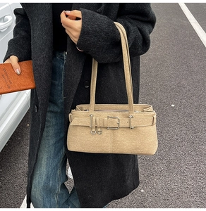 Close-up of beige shoulder bag with silver buckle and textured finish on a black coat