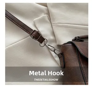Gros plan du crochet en métal bronzé et du cuir marron texturé du sac à bandoulière
