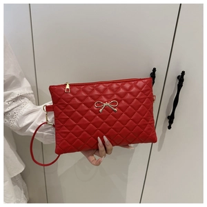 Détail du sac matelassé rouge avec nœud doré et fermeture éclair en métal lisse