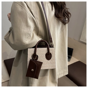 Straw square crossbody bag with brown leather strap shown on a model in a minimalist room