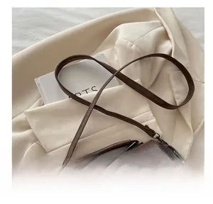 Gros plan d'un sac rétro en cuir marron grainé posé sur un blazer blanc et un livre
