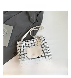 Macro detail of houndstooth tote bag featuring a white leather pocket and cat pendant