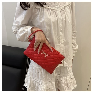 Détail de la pochette matelassée rouge avec fermoir nœud doré portée sur une robe en dentelle