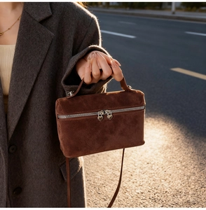 Detail of suede crossbody bag featuring heart-shaped metal zipper pulls and top handle