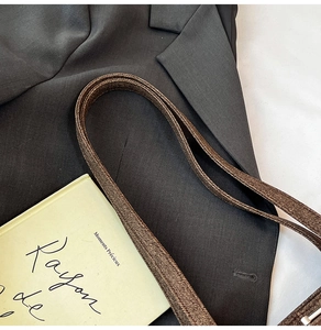 Macro detail of dark brown woven shoulder strap with polished glossy texture on dark blazer