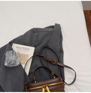 Overhead view of a vintage brown cylindrical leather bag with gold hardware on a gray blazer
