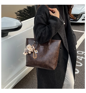 Detail of vintage coffee leather tote bag with plush leopard charm in outdoor setting