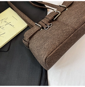 Detail of a brown textured tote bag featuring vintage silver buckles and a rectangle shape