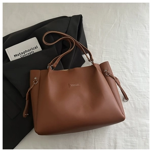Detail of caramel leather tote bag with metal buckle and logo patch on white fabric
