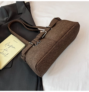 Detail of a dark brown textured fabric underarm bag with decorative metal buckle straps