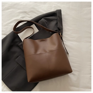 Detailed view of dark brown faux leather bucket bag with wide strap and gold buckle