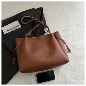 Detail of caramel leather tote bag with decorative patch and side drawstring accents