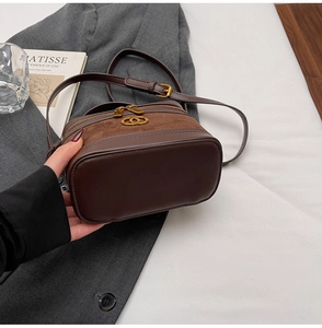 Detail of dark brown leather crossbody bag with gold logo and dual zipper closure