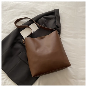 Close-up of a brown minimalist leather bucket bag placed on a grey suit jacket