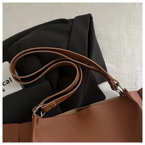 Detail of brown leather tote bag showing silver metal rings and stitching on shoulder straps