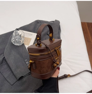 Detail of dark brown leather vanity bag with suede panels and gold shell charms