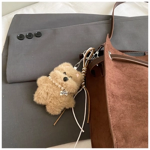 Detail of plush dog keychain with pearl necklace on a brown suede tote bag