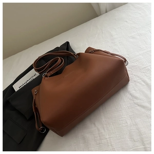 Detail of brown leather tote bag with metallic buckle on textured white bedding