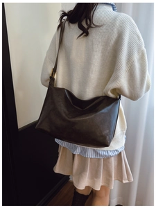 Detail view of large dark brown leather tote bag with wide strap and golden hardware