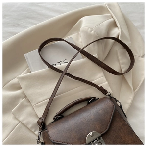 Detailed view of dark brown vintage leather bag with silver metal clasp on a blazer