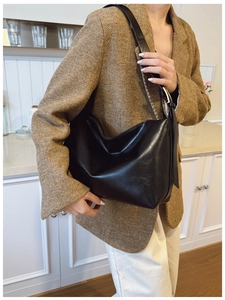 Detail of a large black leather tote bag with metallic buckle and soft textured finish