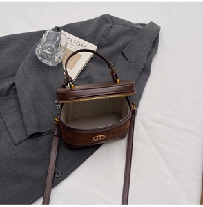 Detail of dark brown leather mini vanity bag with gold logo and suede texture contrast