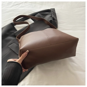 Detailed view of dark brown textured leather tote bag with vertical stitching and wide base