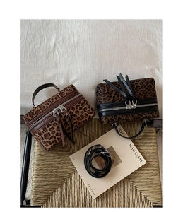 Détail de mini sacs boîte à motif léopard en cuir marron et noir sur une chaise en paille