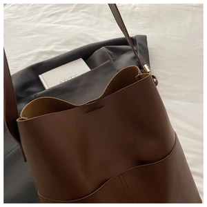 Detail view of brown leather bucket bag showing side pocket and smooth matte texture