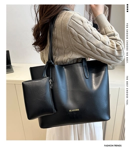 Detail of black tote bag with lychee texture and gold logo shown on model's shoulder