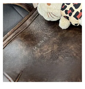 Close-up of vintage oil wax leather tote featuring the metal JUHAI logo and fine stitching