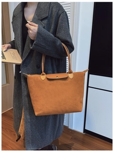 Detail of a brown suede tote bag with leather handles and a classic metal snap button
