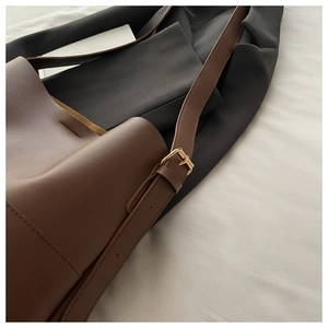 Detailed close-up of dark brown matte leather bucket bag with polished gold buckle