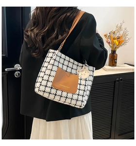 Close-up of black and white houndstooth tote bag with brown leather pocket and cat charm