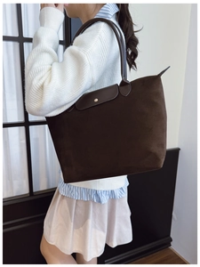 Detail of dark brown tote bag with leather flap closure and gold metal buckle