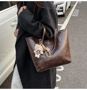 Brown faux leather tote bag featuring crackle texture and a leopard doll charm accessory