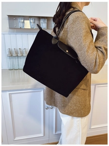 Detail of a black large-capacity tote bag with leather flap and golden snap button closure