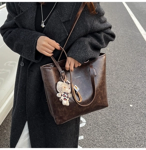 Detail of vintage brown tote bag with cracked leather texture and cute cat charm