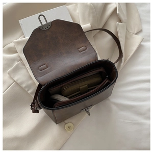 Detail view of the brown leather crossbody bag featuring a metal flip clasp and inner pocket