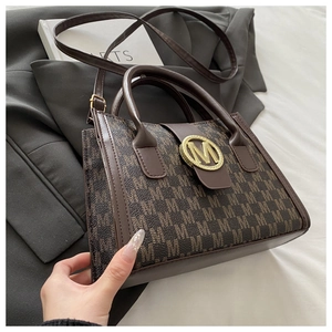 Dettaglio borsa a mano monogramma marrone con logo M dorato su blazer grigio