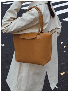 Close-up of brown suede tote bag featuring a leather flap and gold metal button closure
