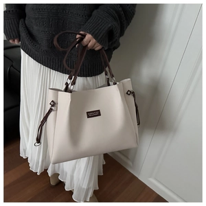 Detail of a large cream tote bag with brown handles and a stylish leather patch
