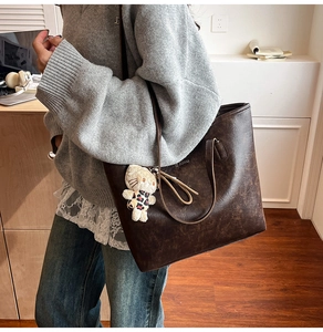 Detail view of large dark brown leather tote bag with brand logo and plush kitten charm