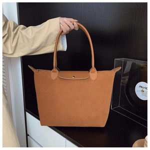 Detail of a brown suede tote bag with leather handles shown against a minimalist wall