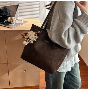 Detail of a large dark brown tote bag with a plush charm on a wooden desk with a laptop
